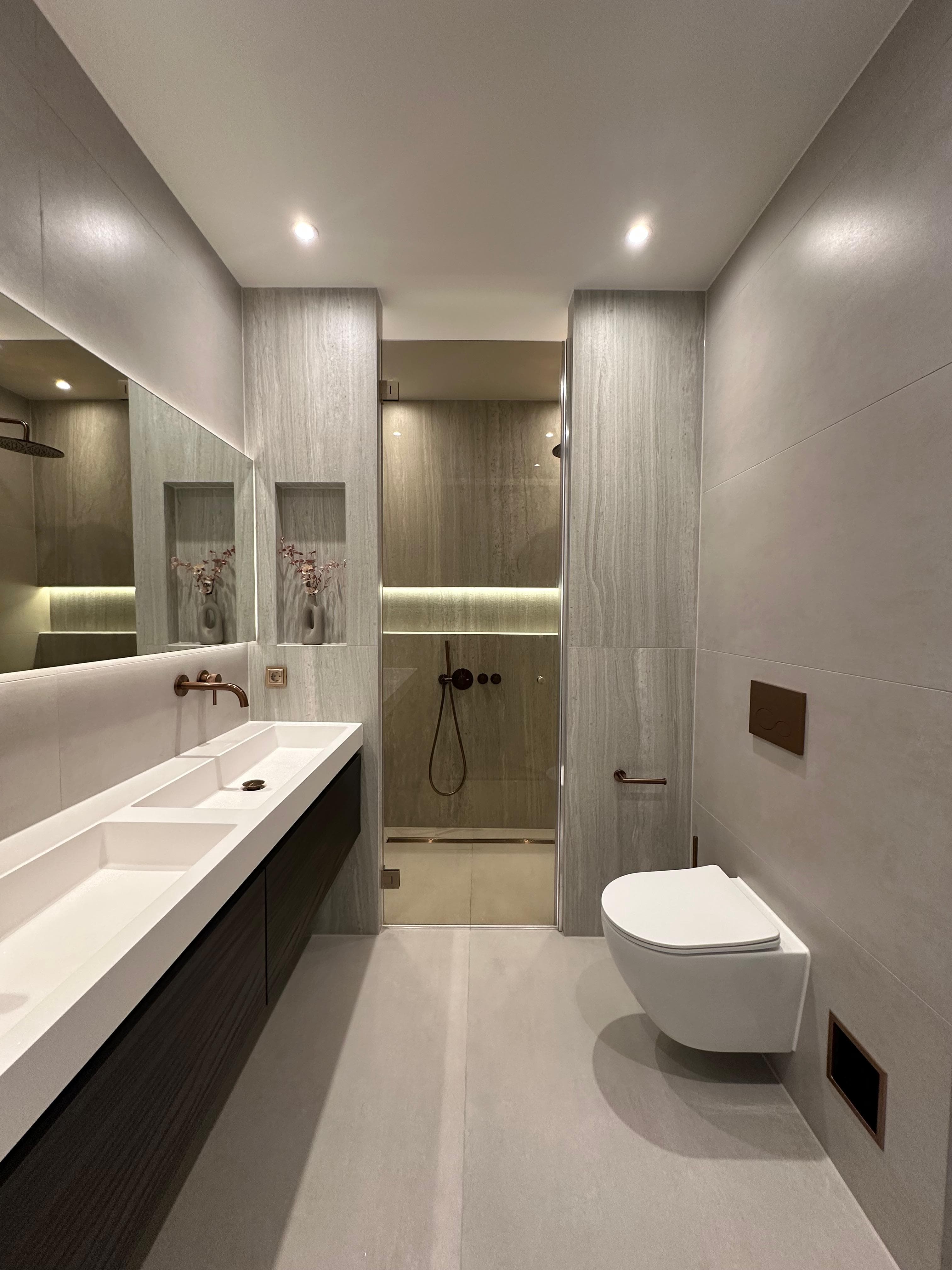 Moderne badkamer met travertijnlook tegels, dubbele wastafel en bronzen kraanwerk, gerenoveerd door SaniTech
